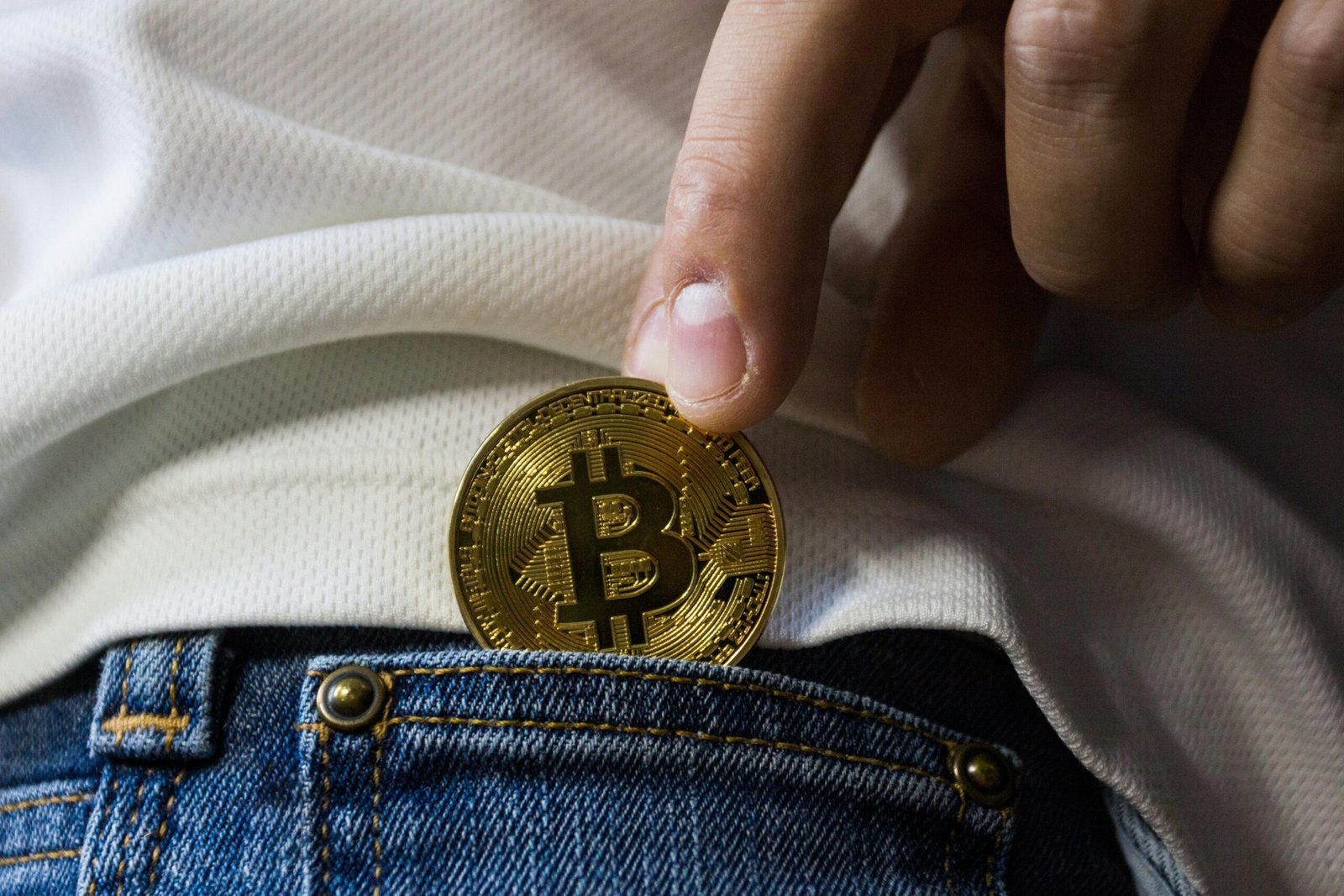 What Is Cryptocurrency? A Simple Beginner Guide (2025) Close-up of hand putting Bitcoin in jeans pocket symbolizing cryptocurrency savings.